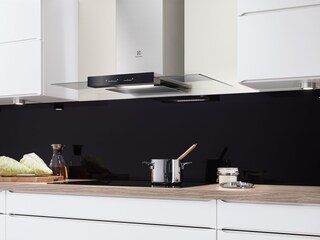 Um exaustor de chaminé em vidro e aço inoxidável por cima de uma placa de indução com um tacho